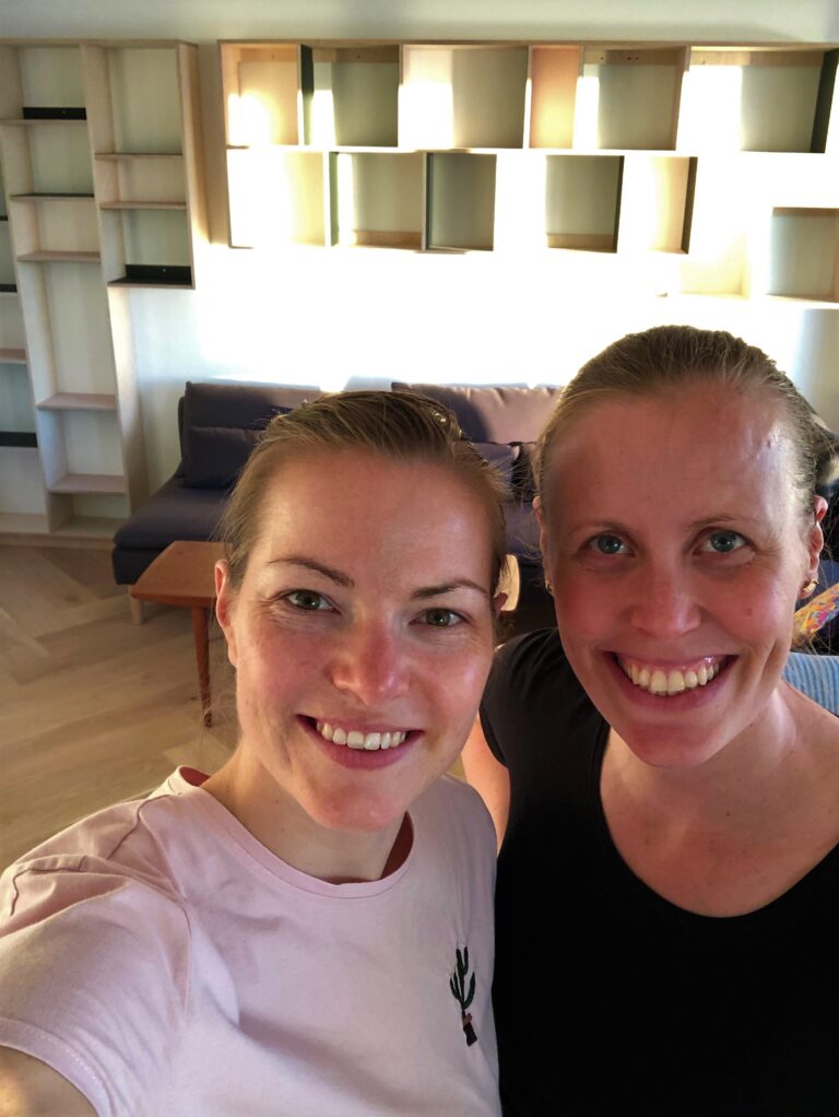 Kamilla og Christinna foran deres specialbyggede reol, som er lavet i birkefiner og linoleum, farverne powder og conifer